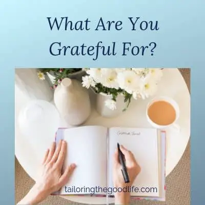 open gratitude journal on round white table with flowers and a cup of tea
