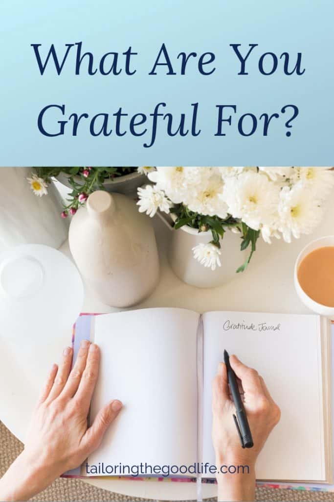 open gratitude journal on round white table with flowers and a cup of tea to work on gratitude journal prompts